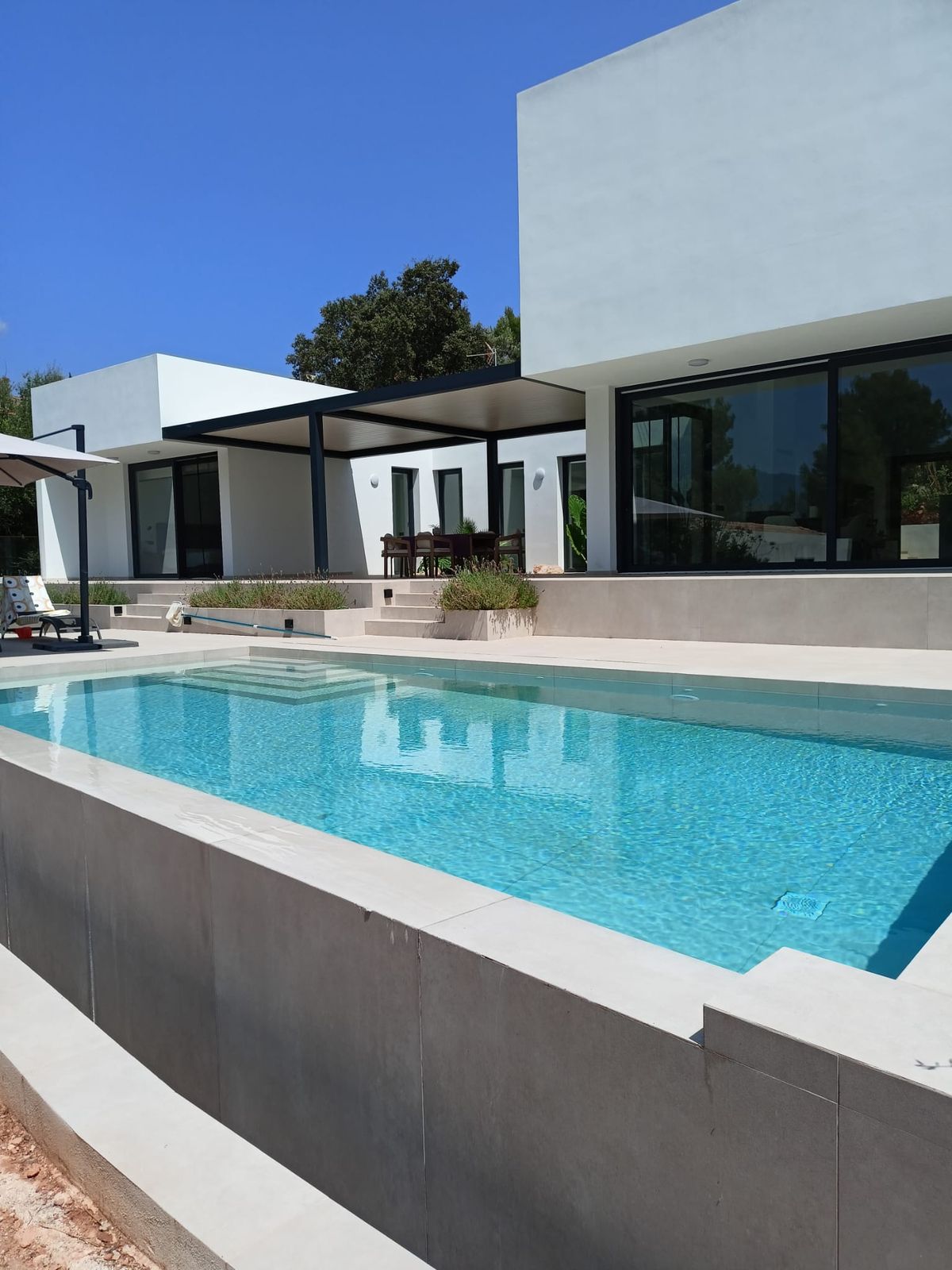Chalet reformado en Mallorca por Las Marquesinas: fachada blanca, ventanales de aluminio negro, pérgola y piscina con coronación de porcelánico
